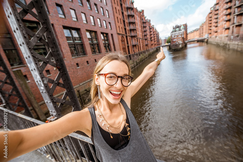 Young woman tourist making selfie photo on the beautiful water channel background in Speicherstadt, historic warehouse district in Hamburg, Germany photo