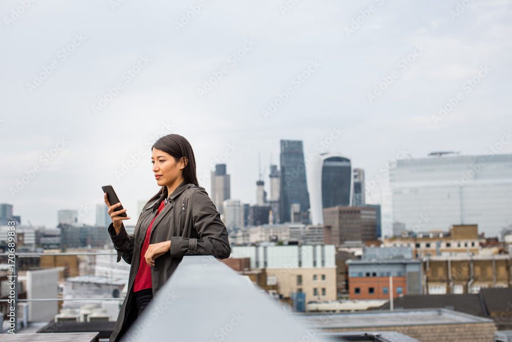 Businesswoman using smartphone with London city skyline