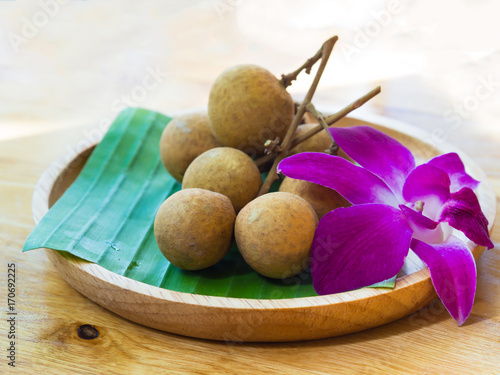 Tropical sweet fruit, Longan with fresh green banana leaf and purple orchid on wooden dish with wooden table background