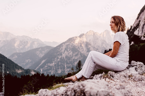 Caucasian tourist sitting on the rock and looking at forest and mountain