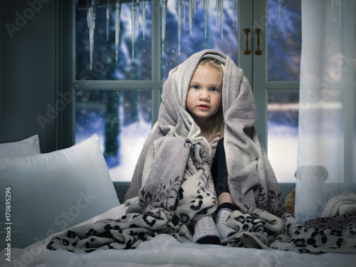 small child wrapped in a blanket on the bed. Children's room window. Outside the window, snow, winter photo