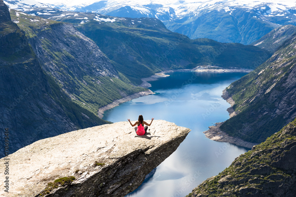 Young woman relaxon Trolltunga. Happy girl enjoy beautiful lake and good weather in Norway.