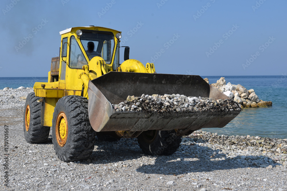 Piles of shingle dumped on the beach shore replenish and widen. Large trucks restore sand on the coast expanding the beach