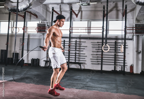Muscular man skipping exercise with jumping rope in gym