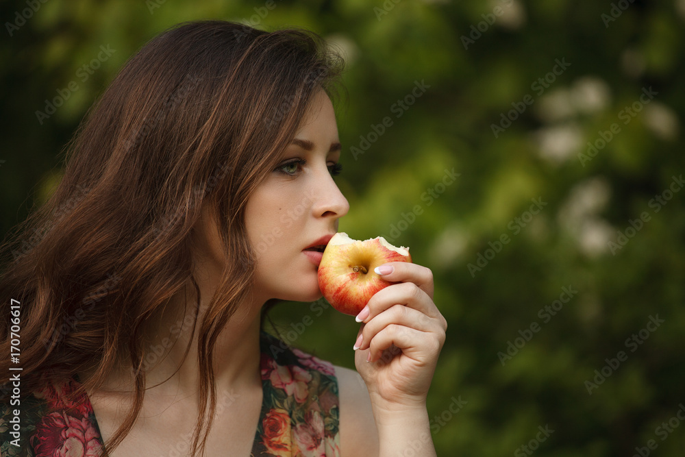 A young beautiful woman holding a ripe apple on a green background A young beautiful woman holding a ripe apple on a green background