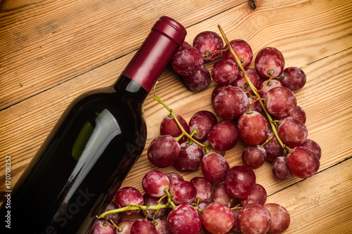 Botella de Vino tinto y uvas moradas sobre mesa de madera rústica. Vista superior