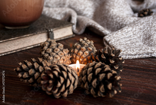 Cup of hot chocolate and warm sweater on wooden rustic bench, Candle and cones, Quiet cozy homely scene. Fall weekend.