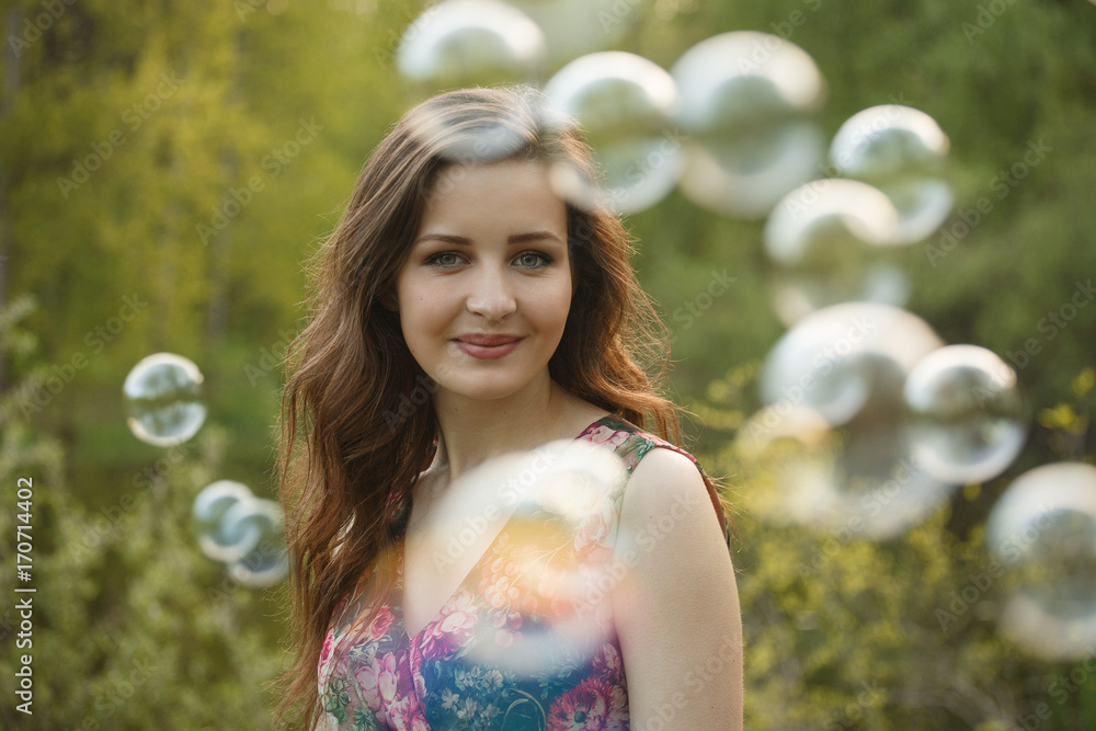 A young beautiful woman is surrounded by  soap bubles in the sunlight