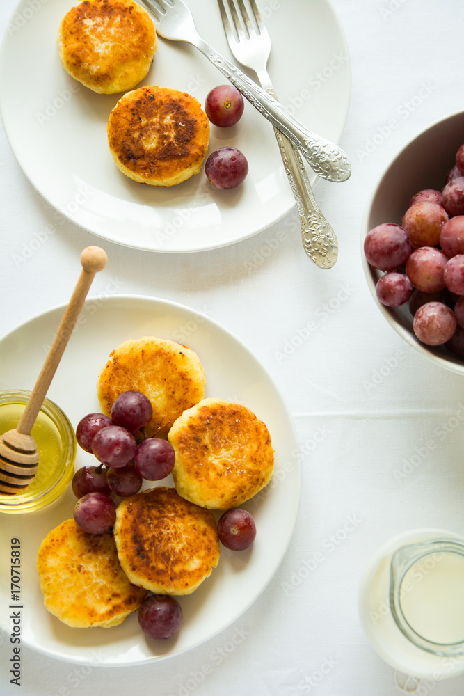 Breakfast with mini cheesecakes, grapes, cream and honey on a white plate Breakfast with mini cheesecakes, grapes, cream and honey on a white plate