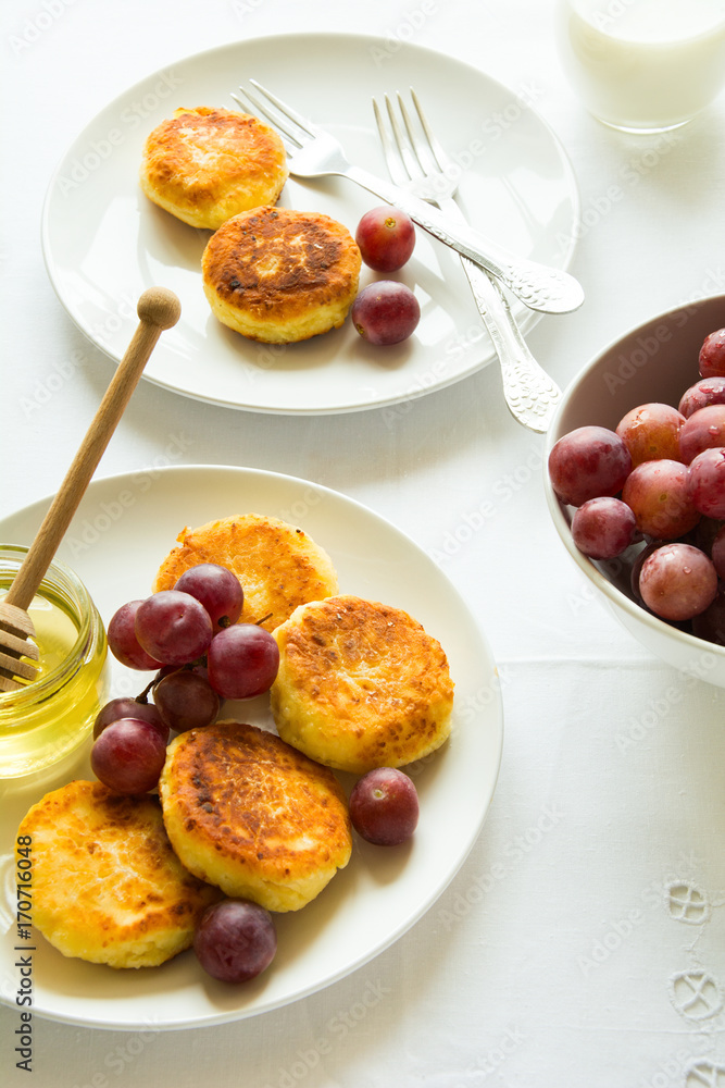 Breakfast with mini cheesecakes, grapes, cream and honey on a white plate Breakfast with mini cheesecakes, grapes, cream and honey on a white plate