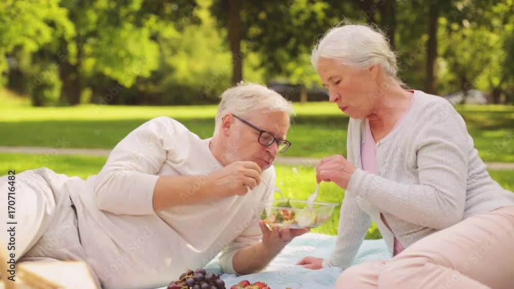 senior couple eating salad at picnic in park senior couple eating salad at picnic in park