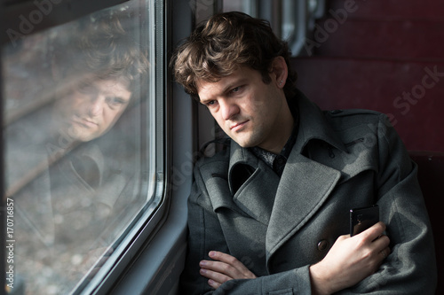 Traveling by train. Sad man traveling by train, looking through the window and thinking about unrequited love squeezing the phone in his hand. alone in an empty train wagon. Real people series. photo