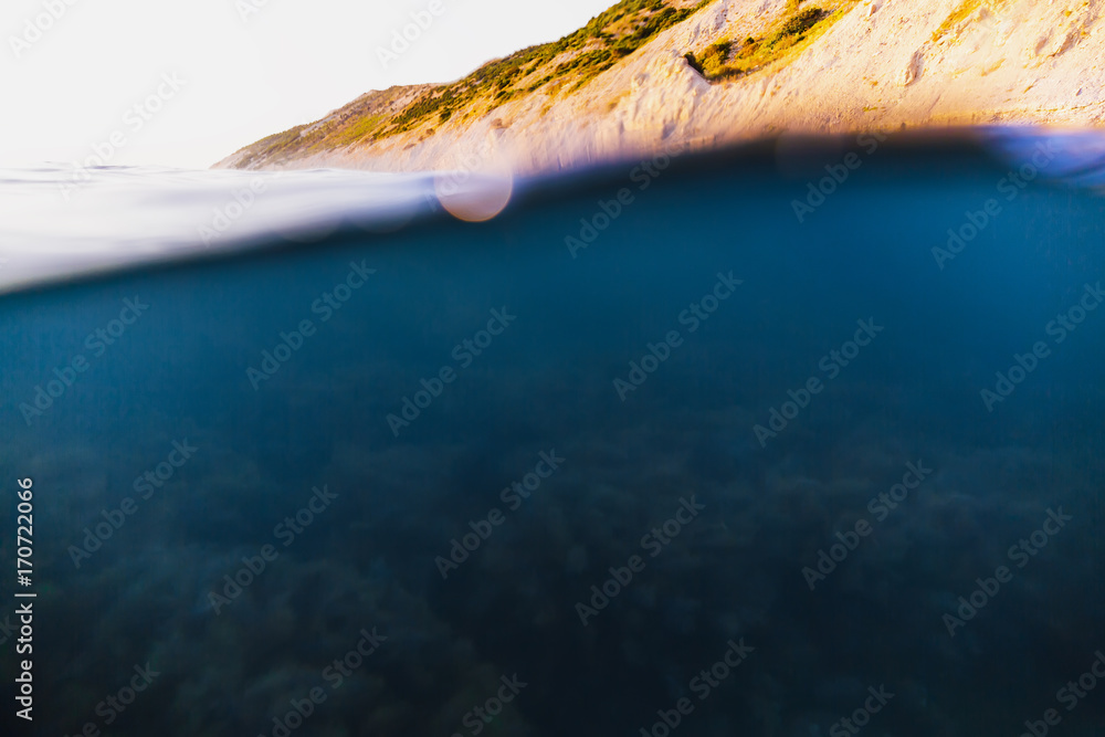 Underwater wave in ocean. Tropical sea with sunset light and rocks. 