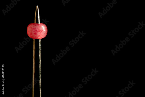 Metal needle through a pink bead, isolated on a black background, macro photo