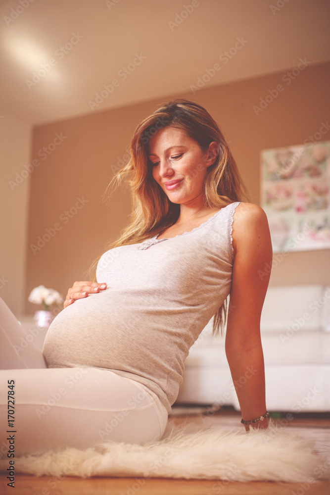 Pregnant brunette woman touching her belly and sitting on floor. Pregnant brunette woman touching her belly and sitting on floor.