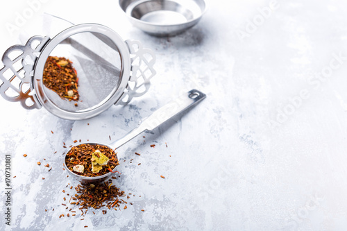 Rooibos tea in a measuring spoon with sieve on light gray background. Healthy drink concept, copy space.
