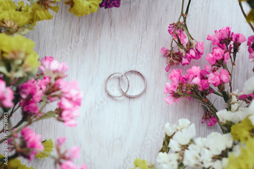 Close-up view of golden wedding rings and beautiful small flowers on wooden tabletop © oleg_ermak
