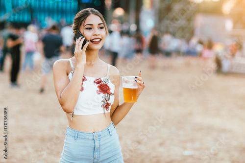 Young woman sitting at music festival and talking on mobile phone 