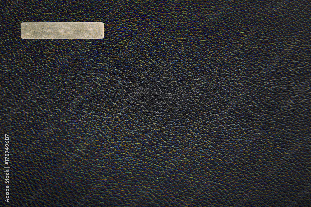Texture of a black leather female bag. A metal label for copy space. Extremely close-up.