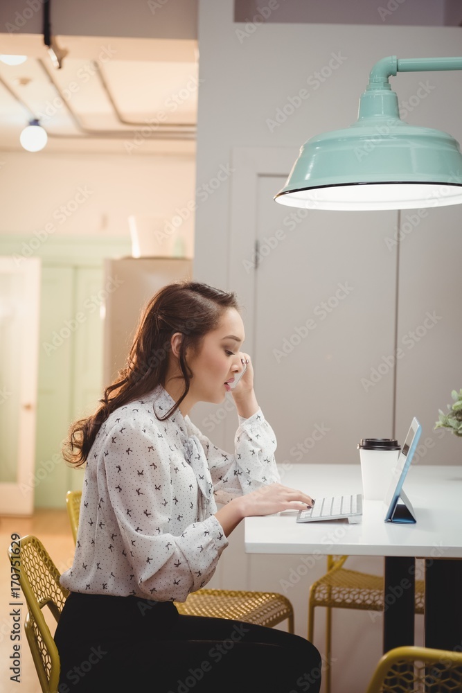 Female executive talking on mobile phone while using digital Female executive talking on mobile phone while using digital