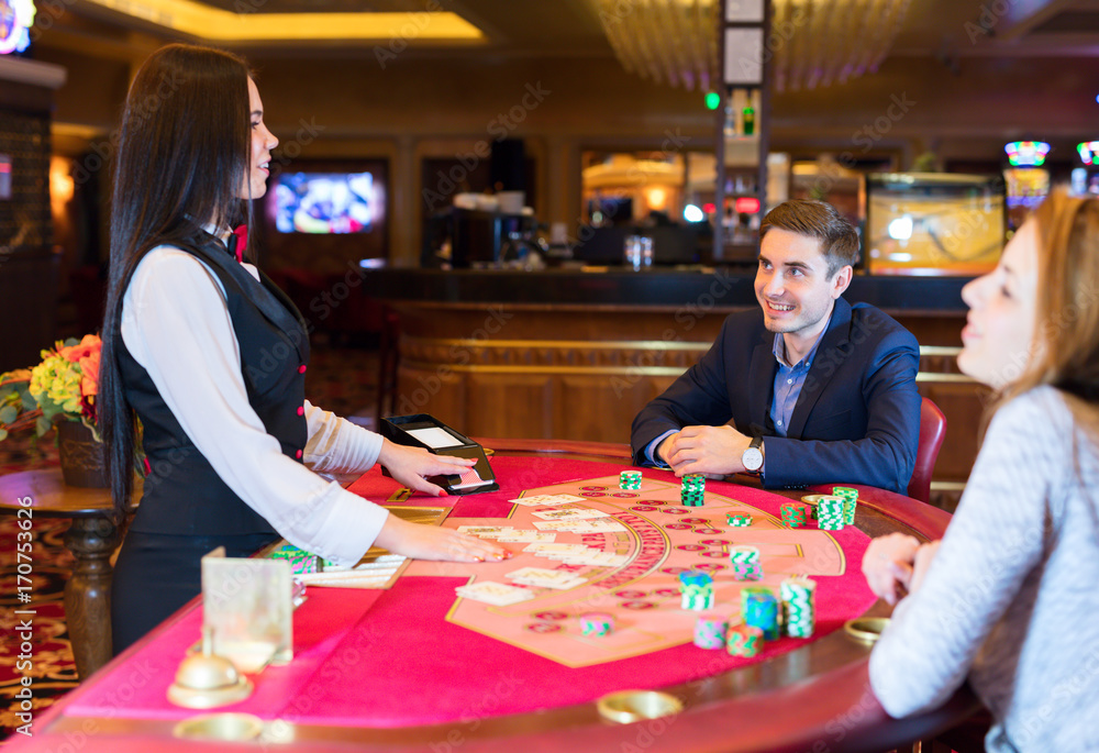 Fototapeta premium Cute lady casino dealer at poker table. Happy couple is playing Black Jack.