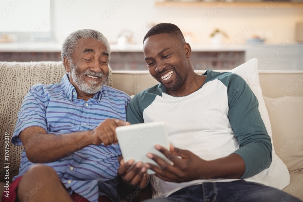 Smiling afro-american father and son using digital tablet in living room - obrazy, fototapety, plakaty 
