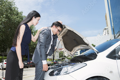 Businessman stressed having trouble with his broken car looking in frustration at failed engine with his girlfriend
