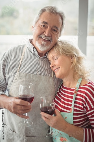 Smiling senior couple holding wine glass in kitchen