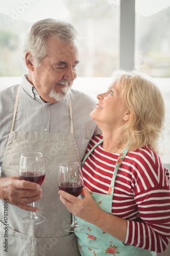Smiling senior couple holding wine glass in kitchen