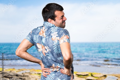 Handsome man with flower shirt with back pain at the beach photo