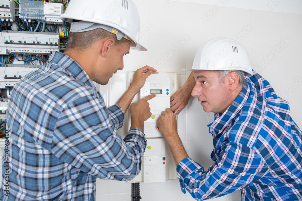 male technicians examining fusebox and thermostat male technicians examining fusebox and thermostat
