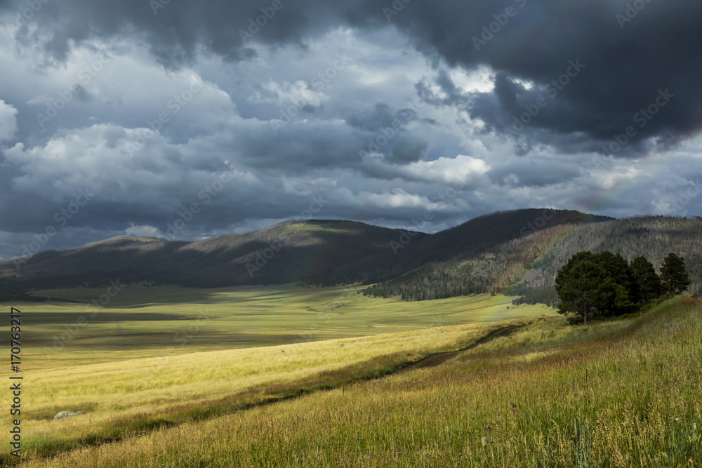 dark storm clouds, sun, and a double rainbow all in one beautiful caldera grassland