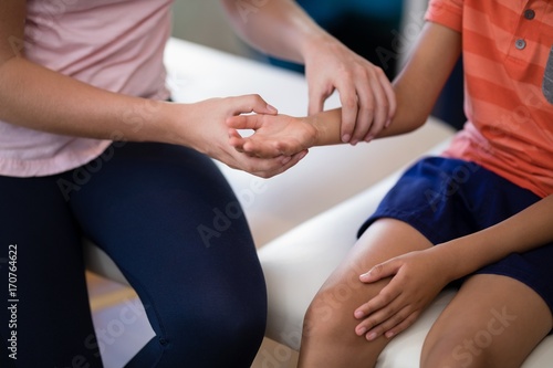 Midsection of female therapist examining wrist with boy sitting