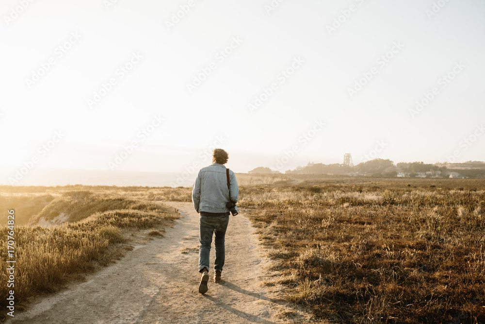 young man walking down path through a field on coast young man walking down path through a field on coast