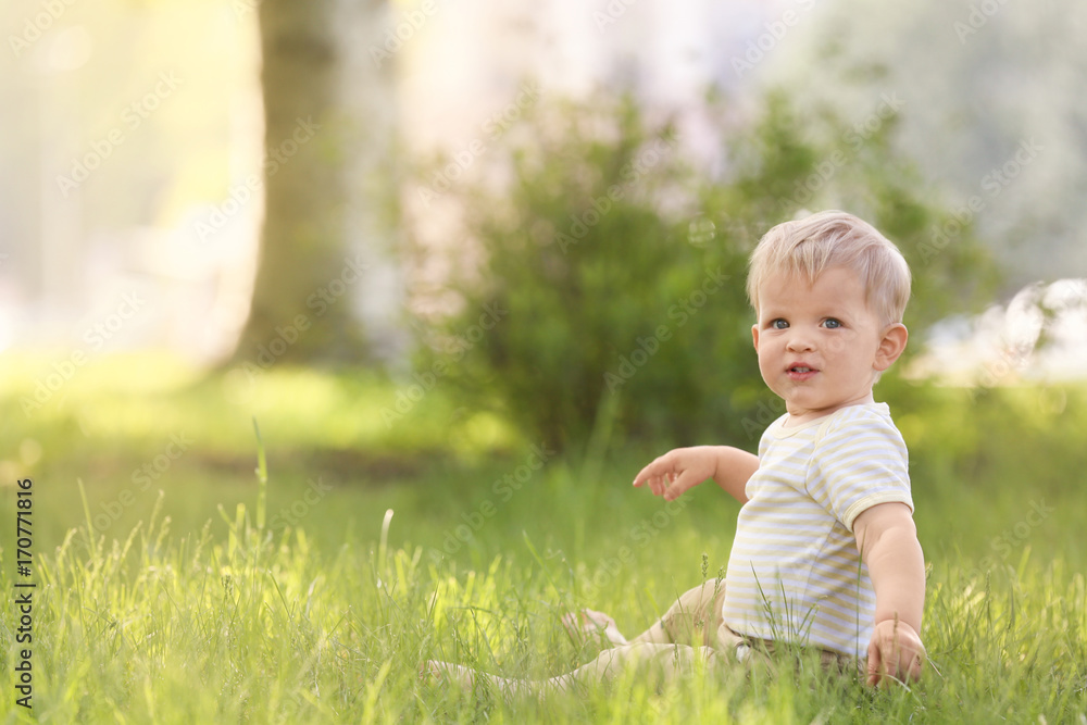 Cute baby boy sitting on green grass in park Cute baby boy sitting on green grass in park