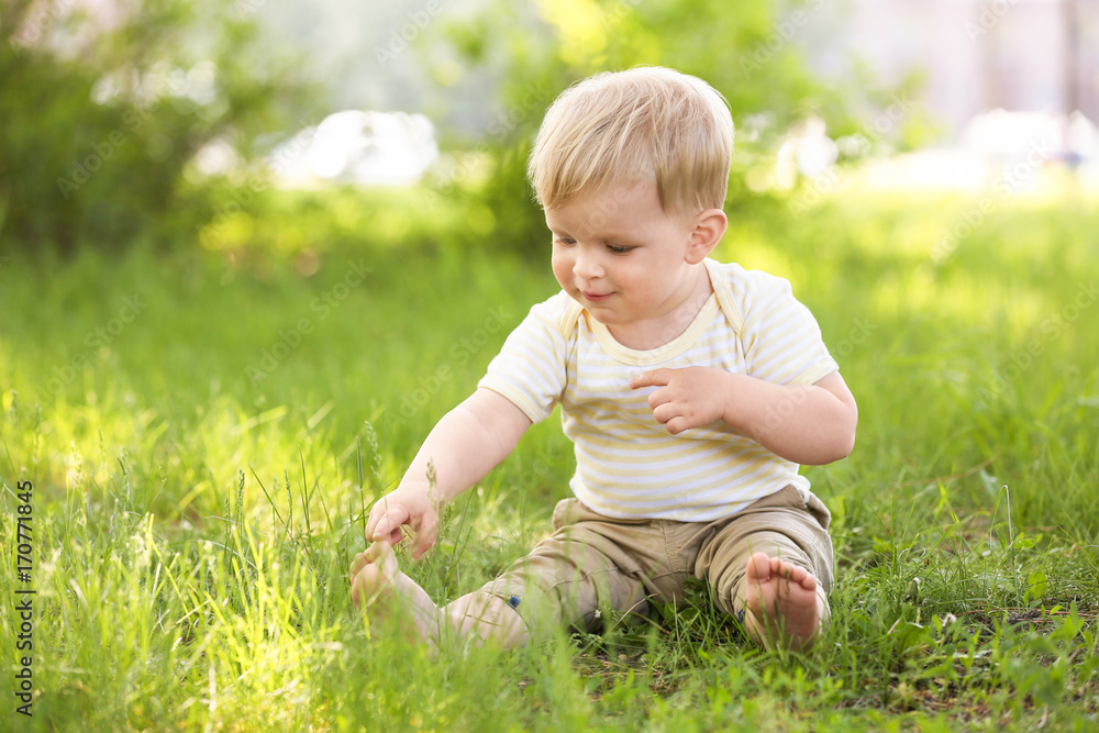 Cute baby boy sitting on green grass in park Cute baby boy sitting on green grass in park