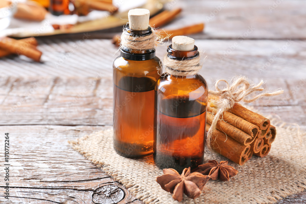 Beautiful composition with essential cinnamon oil in glass bottles on wooden table Beautiful composition with essential cinnamon oil in glass bottles on wooden table