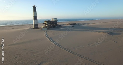 Aerial view footage of desert sand peninsula, old lighthouse and power station building on ocean seals beach, Walvis Bay lagoon view with sea background and ships at Namibia's Atlantic west coast