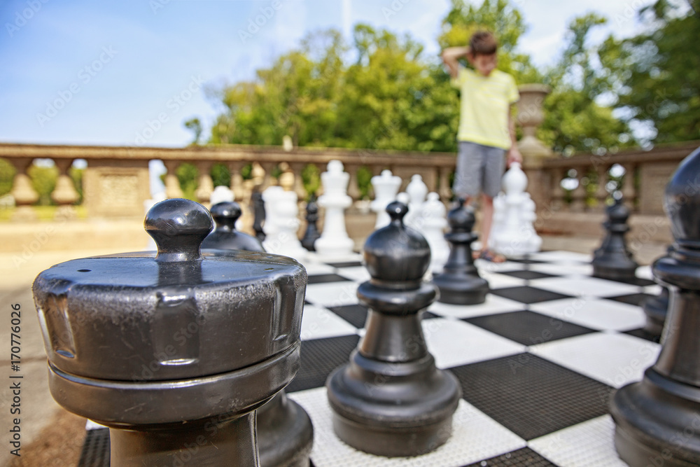 boy reflects on the chess game. large outdoor chess and young player. Blurred background