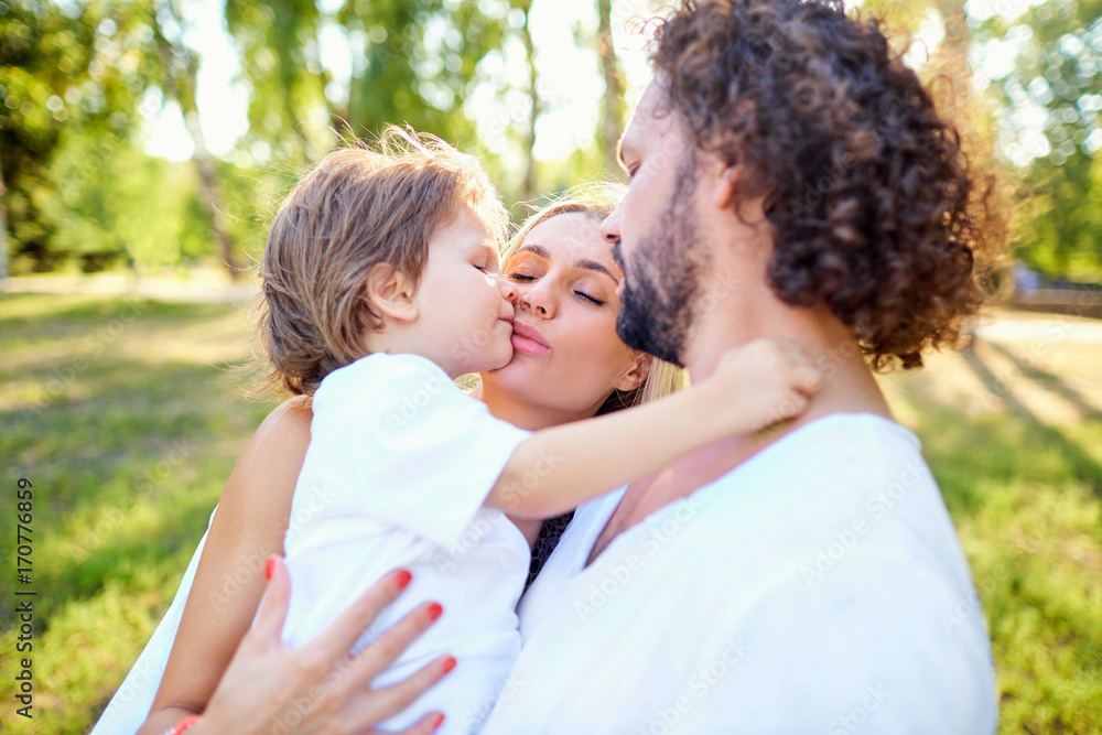 Mother and father hugging a child in the park in the summer. A happy family autumn. Mother and father hugging a child in the park in the summer. A happy family autumn.