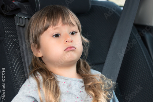 A beautiful little girl is sitting in the car wearing a seat belt. Safety and protection of children. Portrait.