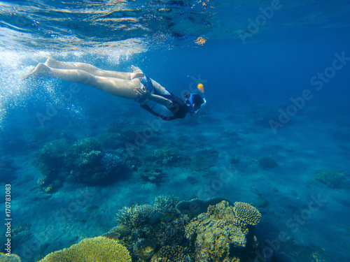 Snorkeling girl in full-face snorkeling mask. Coral reef in shallow sea.