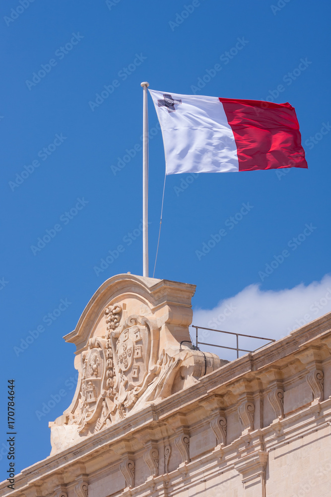 maltese flag on ornate building facade with coat of arms