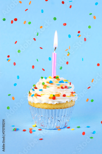 Iced birthday cupcake with with lit candle and sprinkles