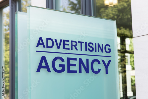 Foto Advertising agency sign on glass board outside building in city