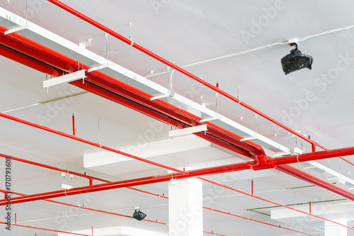 Fire sprinkler system with red pipes is placed to hanging from the ceiling inside of an unfinished new building.