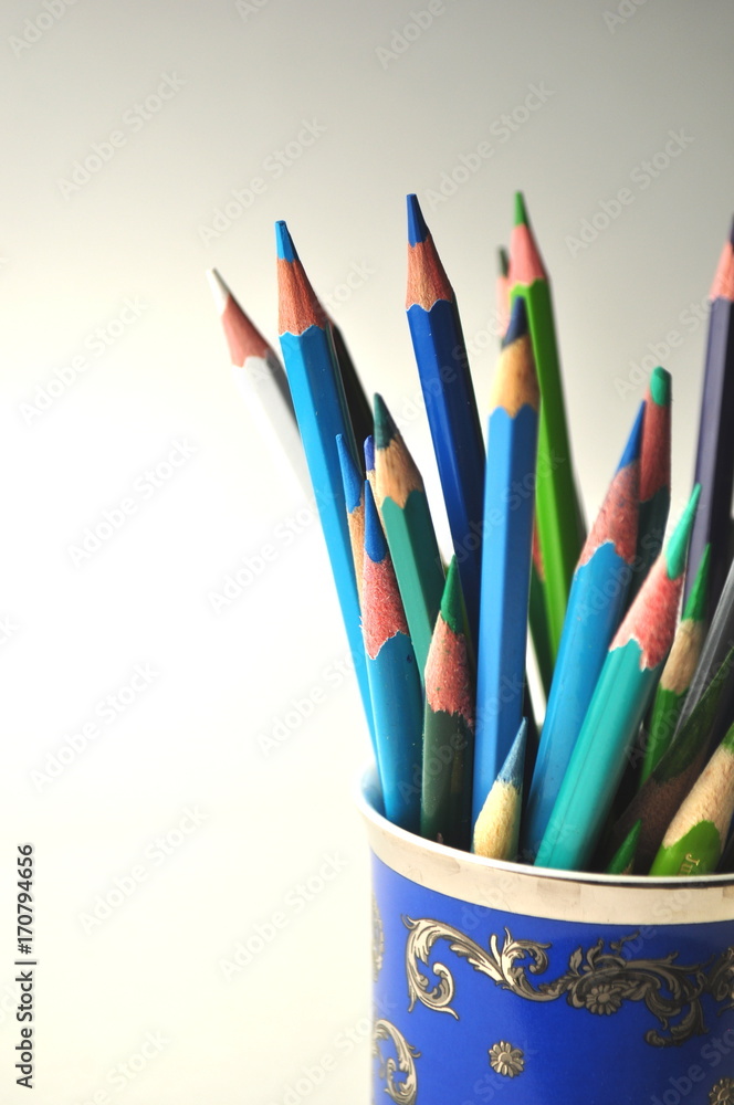 Styled stock image of blue and green color pencils in a blue china cup on grey with copy space Styled stock image of blue and green color pencils in a blue china cup on grey with copy space
