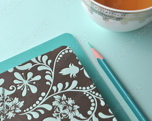 Cup of tean with floral notebook and teal pencil on mint photo