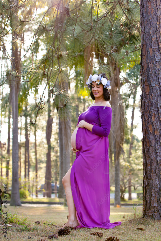 Beautiful pregnant woman in sheer purple maternity dress outdoors under trees