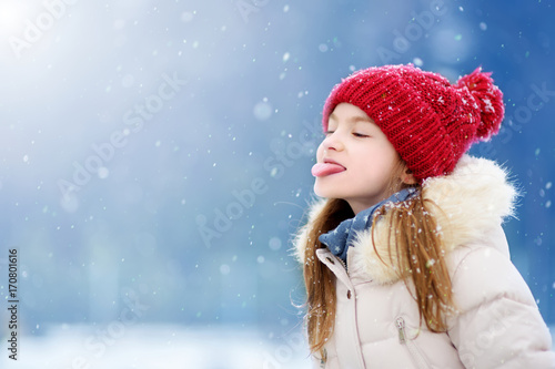 Adorable little girl catching snowflakes with her tongue in beautiful winter park. Cute child playing in a snow. photo
